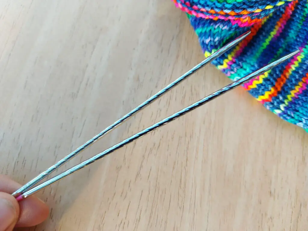 A close up of Addi unicorn twisted needle tips. A partly-knitted sock is in the photo for context
