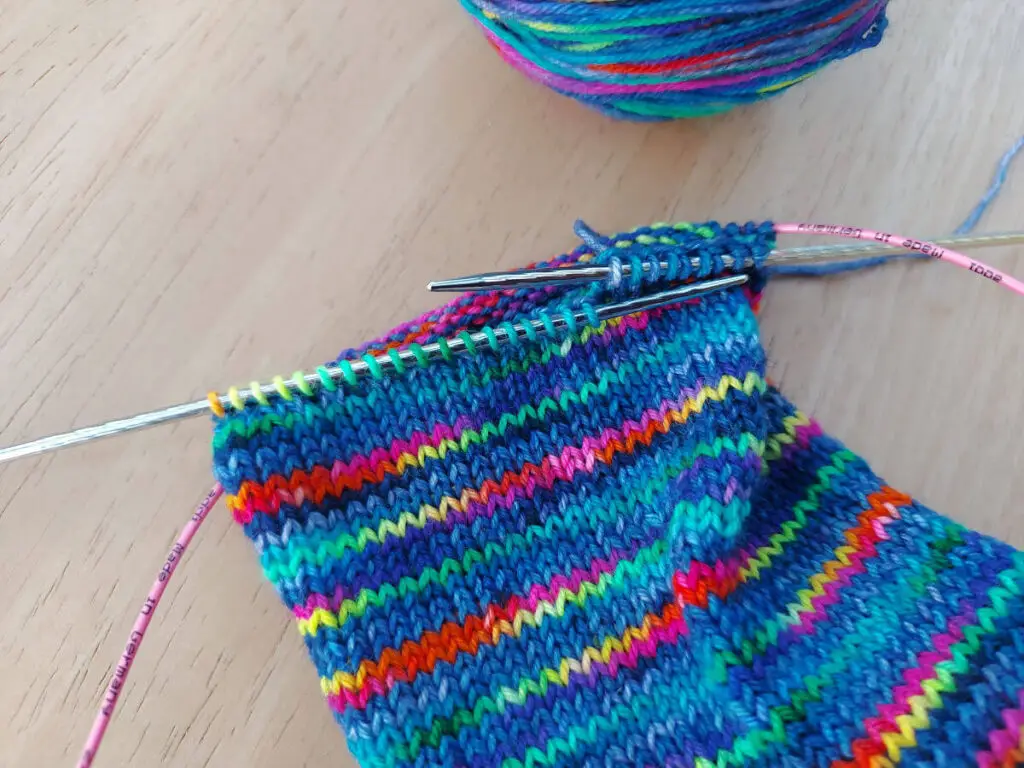 A partly-knitted multicoloured sock on a long circular needle.