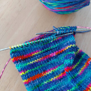 A partly-knitted multicoloured sock on a long circular needle.