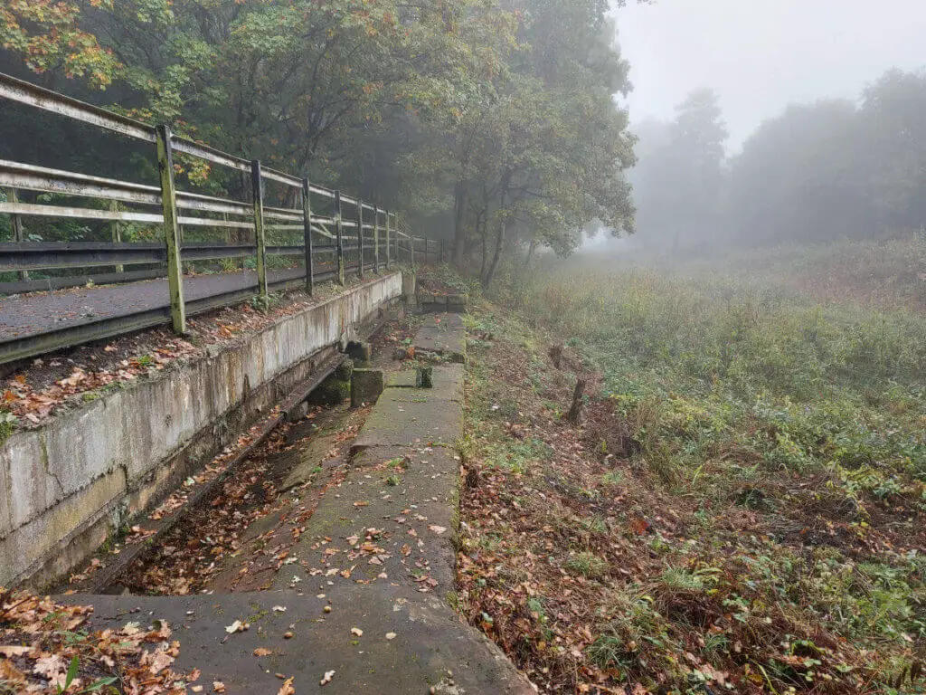 An old stone canal wall lying below the more recent footbridge. The land to the right of the wall used to be a canal but is now overgrown.