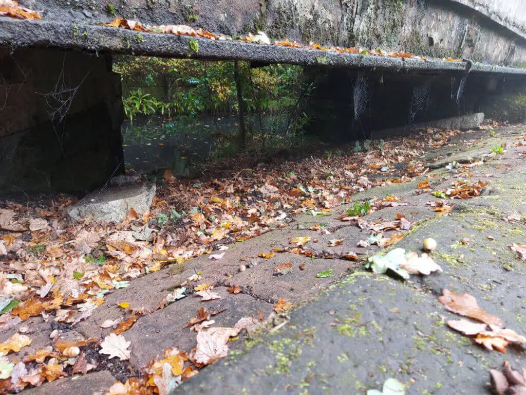 A brick slope which leads to an overflow channel underneath a modern bridge
