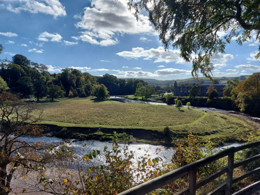 A view across the river and a meadow to the ruins of Bolton Abbey