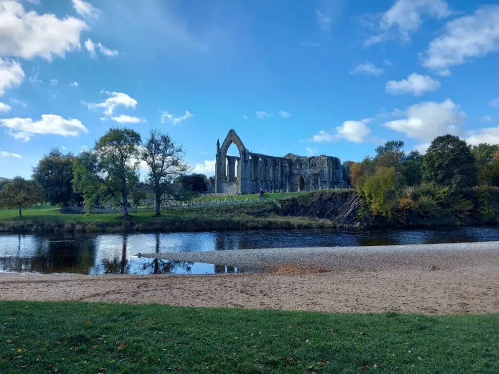 A view across the river and the pebble beach to the remains of Bolton Abbey on a hill