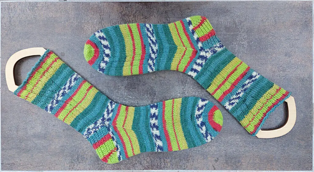 A pair of patterned socks in stripes of shades of green and red on sock blockers lying on a brown shiny tile