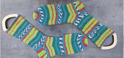 A pair of patterned socks in stripes of shades of green and red on sock blockers lying on a brown shiny tile