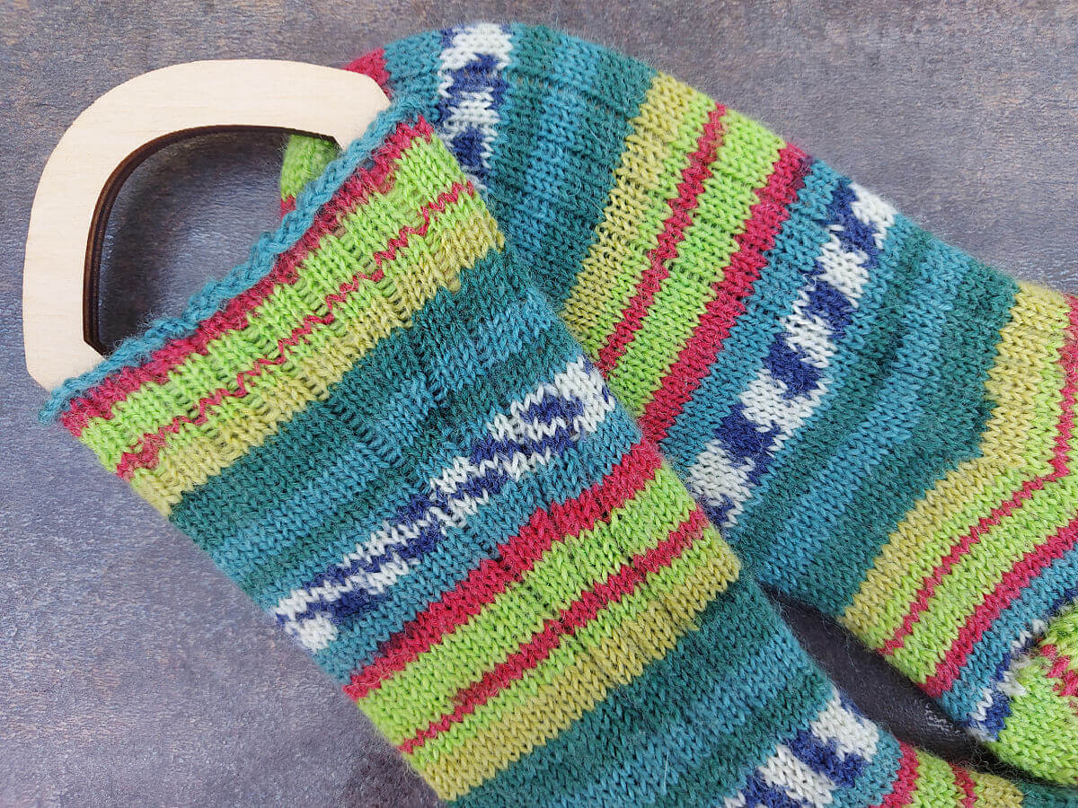 A close up of the rib detail of a pair of a hand knitted socks in stripes of teal, neon green, red and mustard
