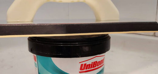 A tub of grout with a grout spreader balanced across it in a shower