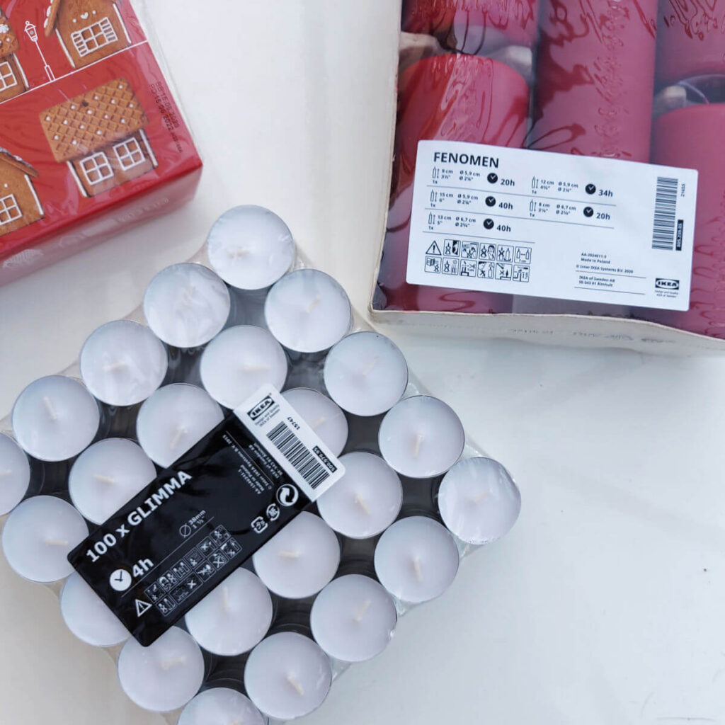 A packet of tea lights, a packet containing red candles and the corner of a gingerbread house kit lying on a white high gloss table