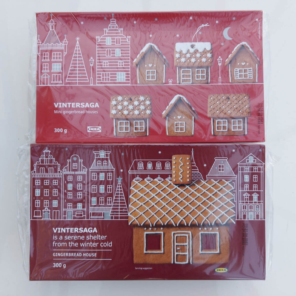 Two red packets containing gingerbread house kits. The top packet contains six small houses and the bottom packet contains one large house