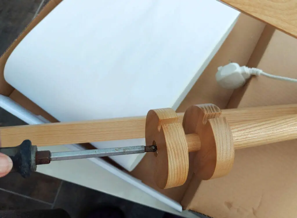 A screw being tightened on a wooden lamp base