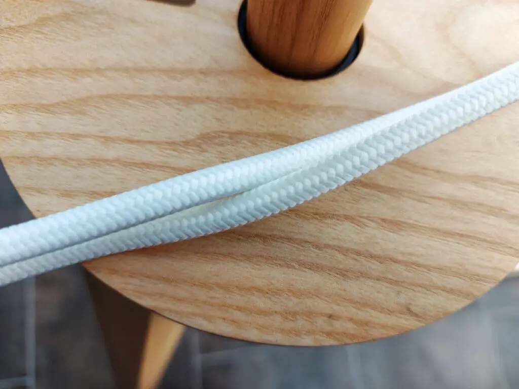 A white woven electricity cable against a wooden lamp stand