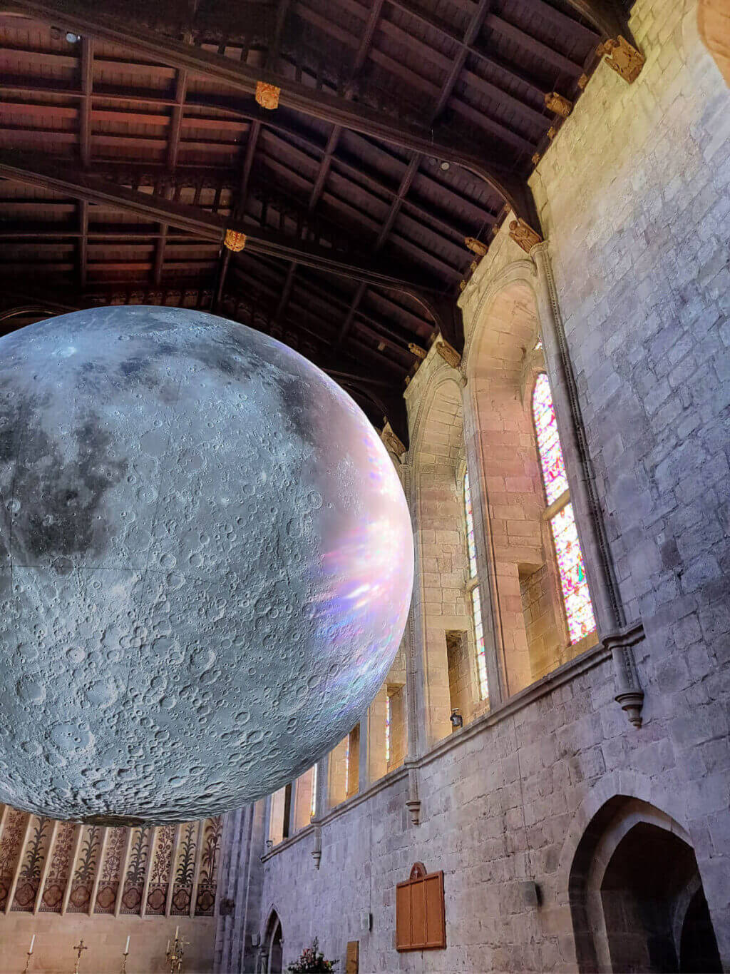 A partial view of the Luke Jerram moon against the wooden ceiling and stone walls of Priory Church, Bolton Abbey