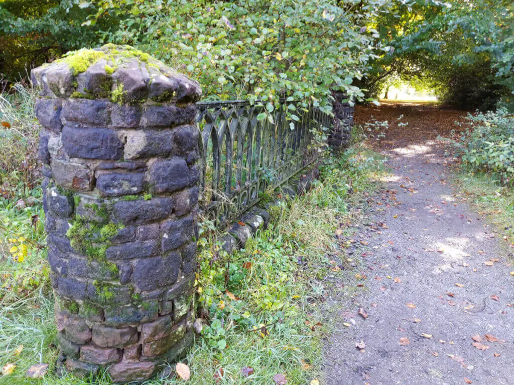 A close up of a circular stone gate post next to a wrought iron decorative fence