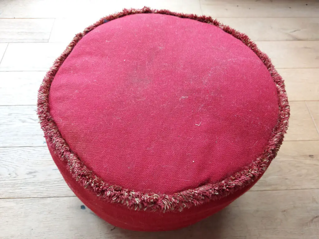 A red pouffe with a short tasselled trim