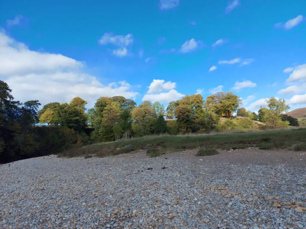 A pebble river beach surrounded by trees in autumn colours