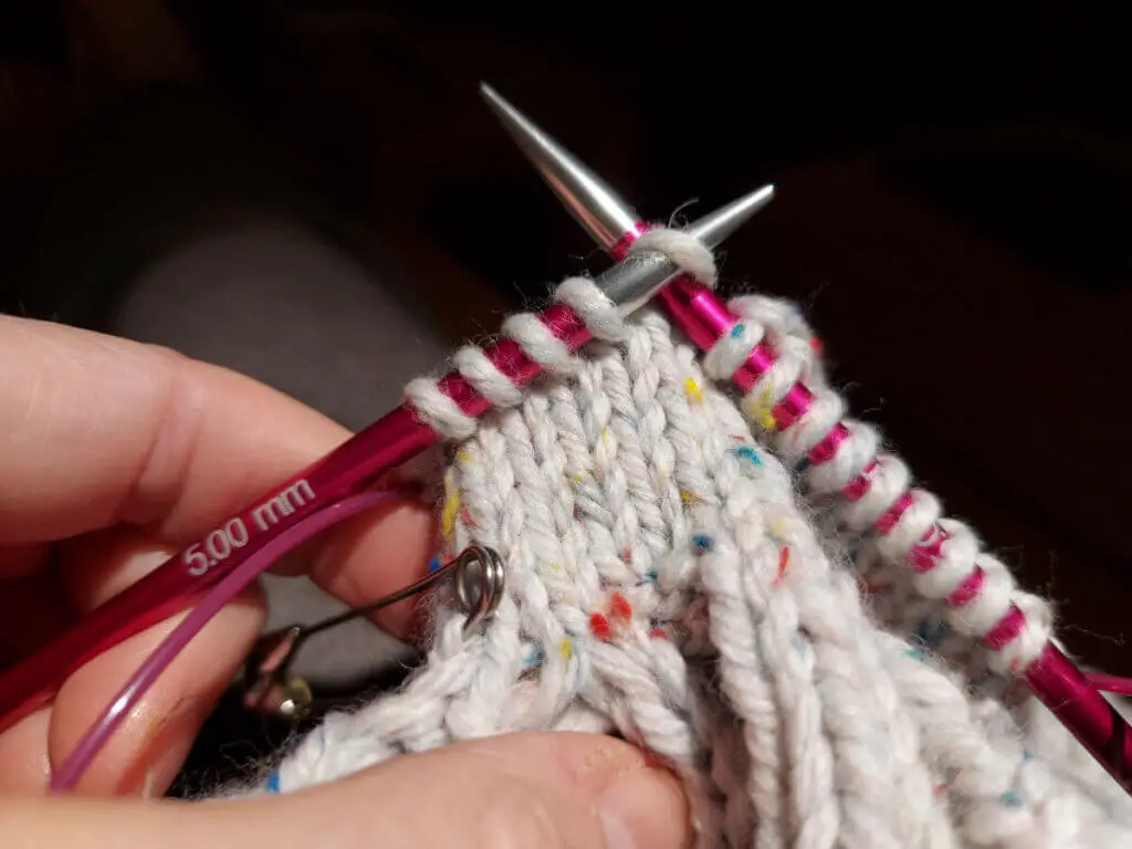 A partly-knitted mitten on pink needle tips