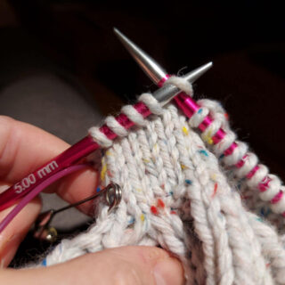 A partly-knitted mitten on pink needle tips