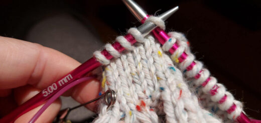 A partly-knitted mitten on pink needle tips