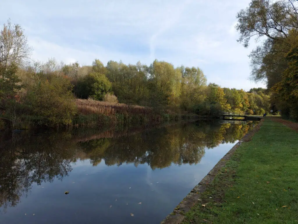 Looking back along the tow path of a canal at the reflections of the trees in the water