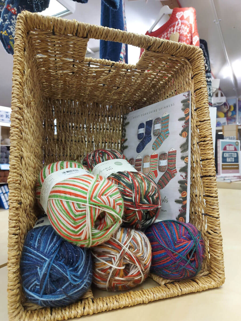 A basket containing multi-coloured balls of yarn and a pattern book