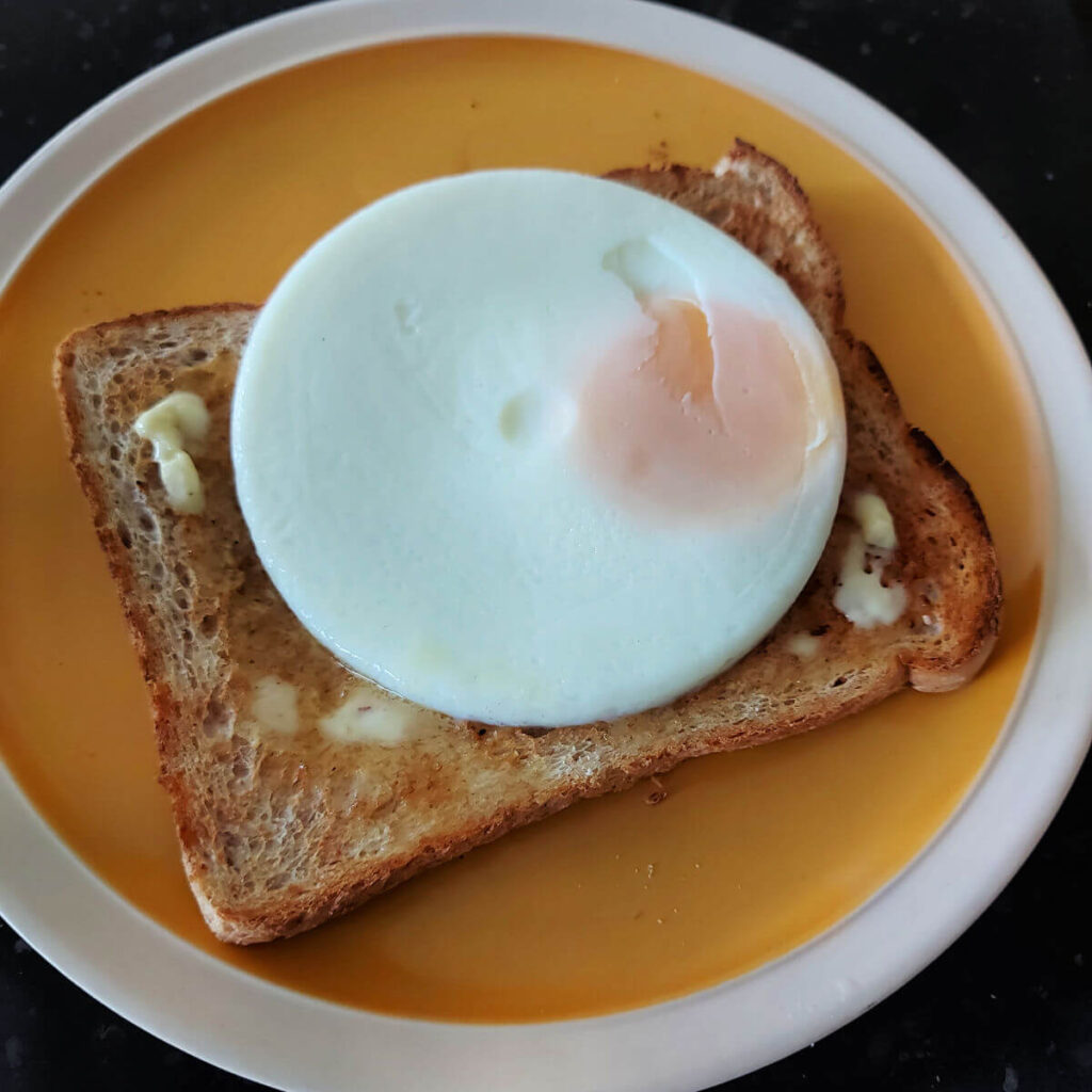 A round, flat poached egg on a piece of toast on a yellow plate