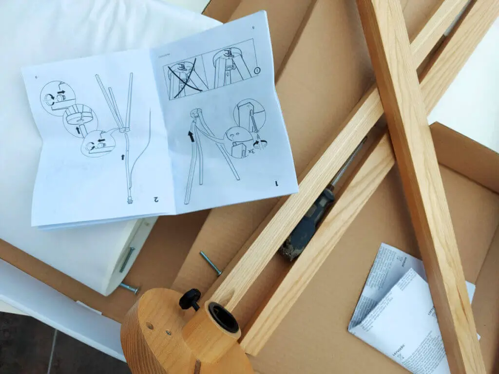 Pieces of a wooden self-assembly lamp lie on a cardboard box next to an instruction leaflet (which is upside down)