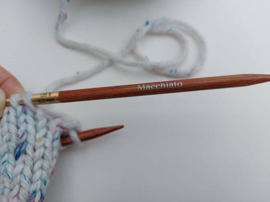 A wooden needle tip with the word "macchiato" stamped on it in silver lettering
