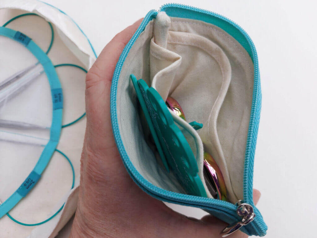 Looking inside an accessories pouch to see a needle gauge, stitch markers and scissors