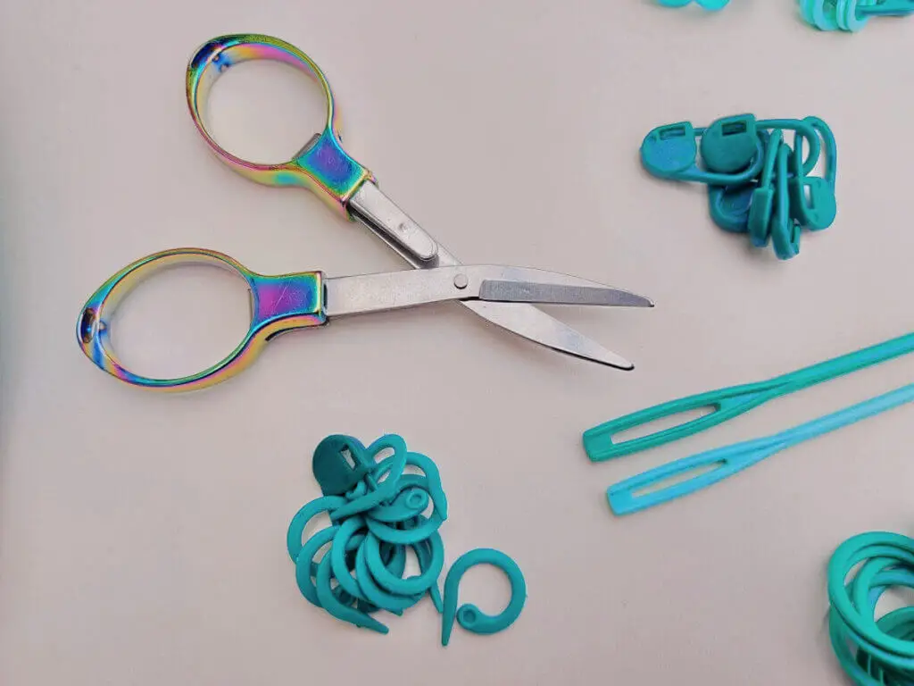 A pair of rainbow-coloured folding scissors opened out to show the blades.