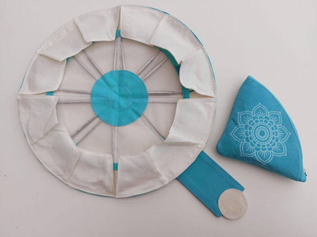 A circular needle case with a small turquoise triangular zipped pouch next to it.