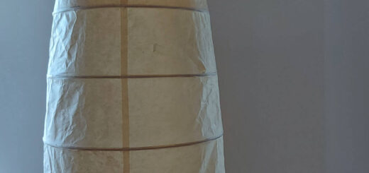 A tall lampshade with a yellowed paper shade stands against a cream wall with a pink Celtic knot tapestry on it