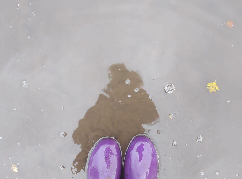 A photo of Christine's reflection in a puddle; she's wearing purple wellies