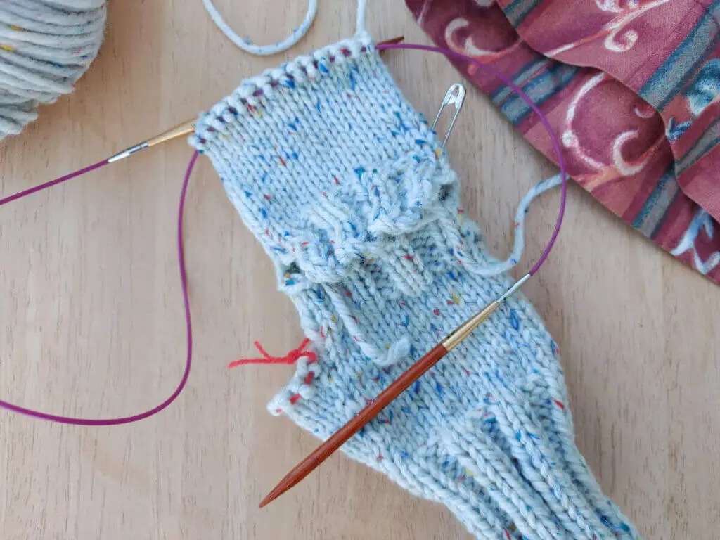 A partly-knitted mitten in off-white yarn with coloured flecks