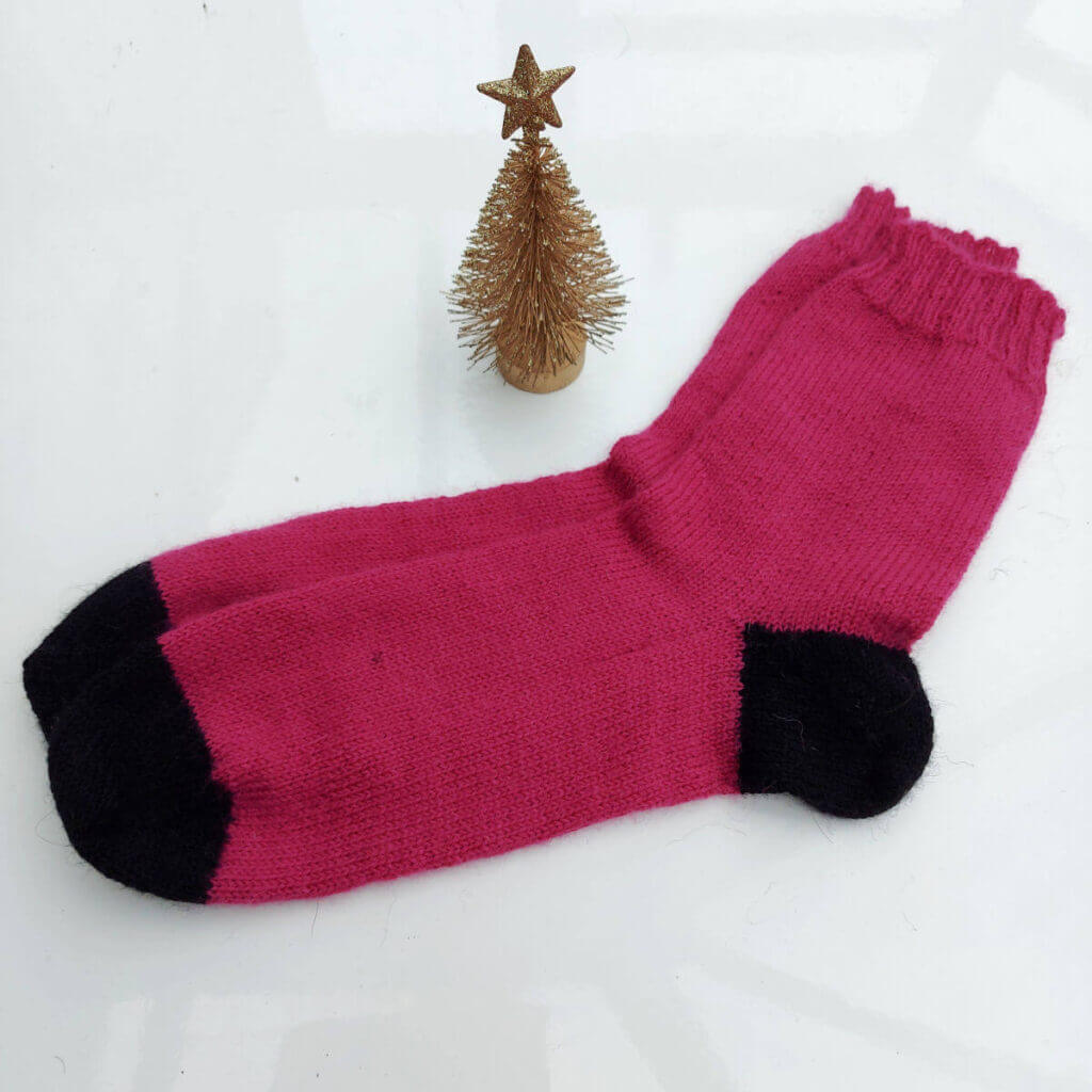 A pair of pink socks with black heels on toes are lying on a white high gloss table next to a small golden Christmas tree ornament