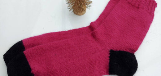 A pair of pink socks with black heels on toes are lying on a white high gloss table next to a small golden Christmas tree ornament