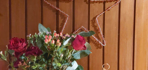 A large star decorated with berries hangs on a wood-panelled wall. Below is a vase of flowers and a bronze-coloured Christmas decoration