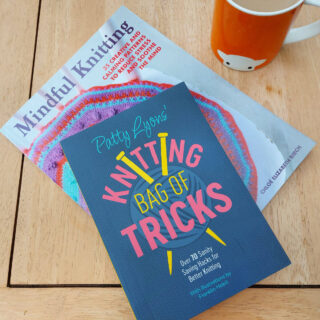 Two books - Mindful Knitting and Patty Lyons' Knitting Bag of Tricks lie on a wooden coffee table next to an orange mug of tea