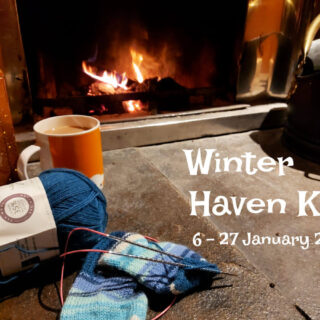 A partly-knitted sock and an orange mug in front of an open fire. Words on the photo read "Winter Haven KAL 6-27 January 2023"