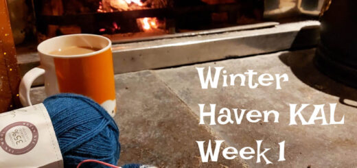 A partly-knitted sock and an orange mug in front of an open fire. Words on the photo read "Winter Haven KAL Week 1"
