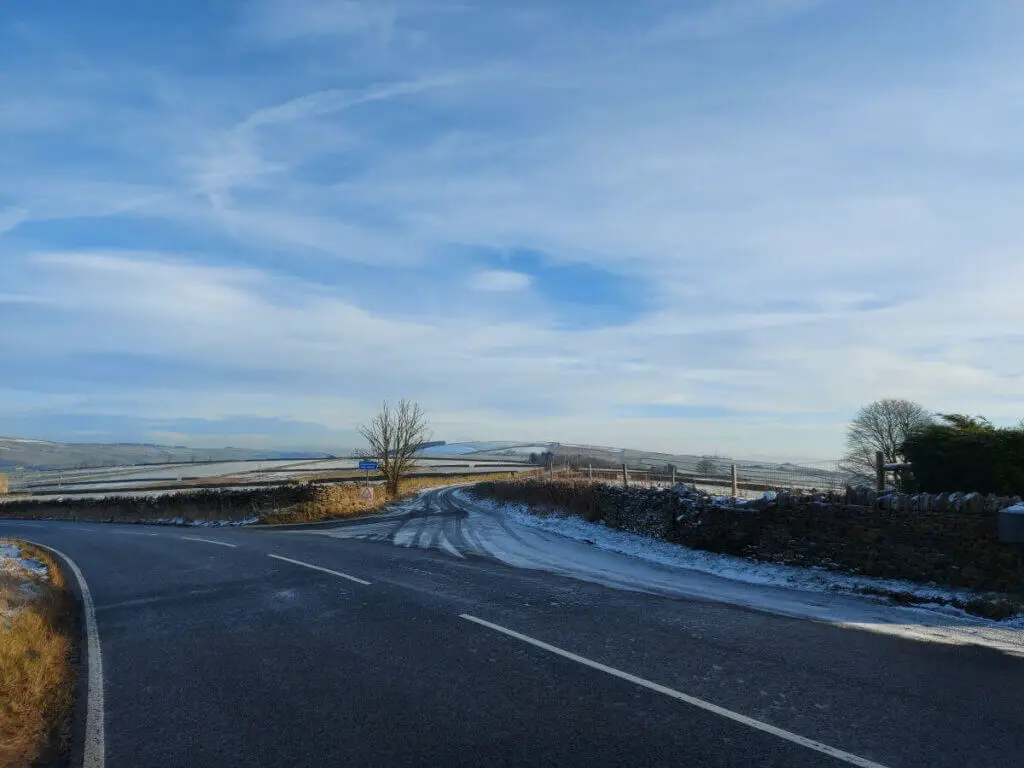 A view across a moorland road.  It's icy and the sky is blue