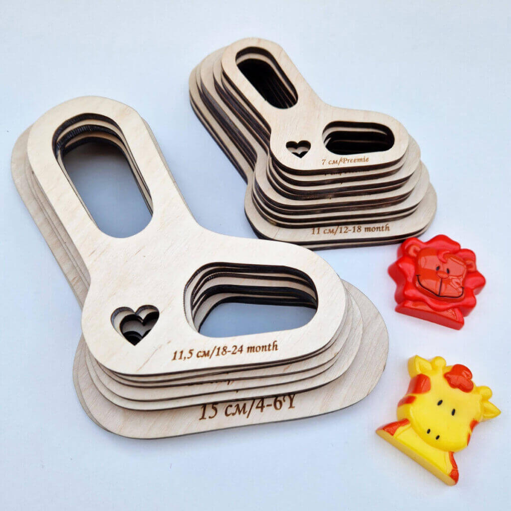 A flatlay showing two stacks of child-sized wooden sock blockers on a white background. There is an orange lion toy and a yellow giraffe toy next to the blockers