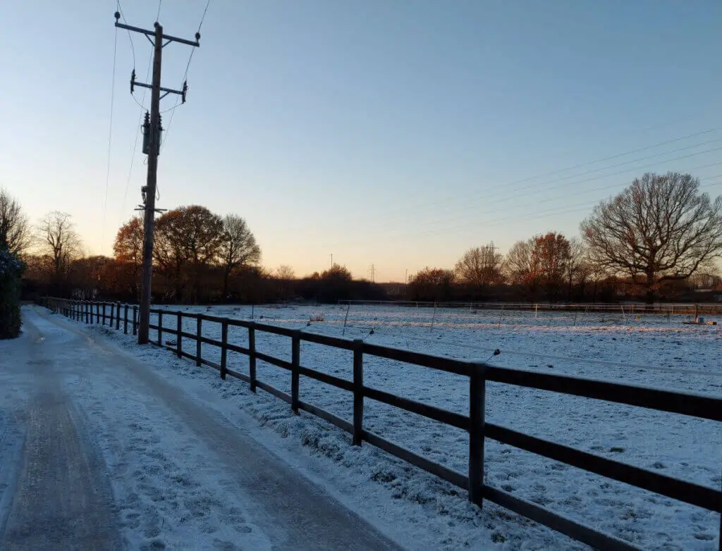 An icy footpath next to a fenced field. There is an electricity pole next to the lane
