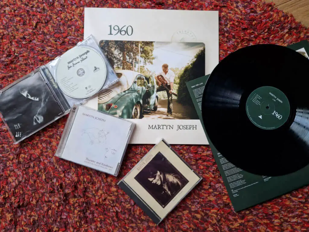 A selection of CDs and a vinyl record spread out across a red rug