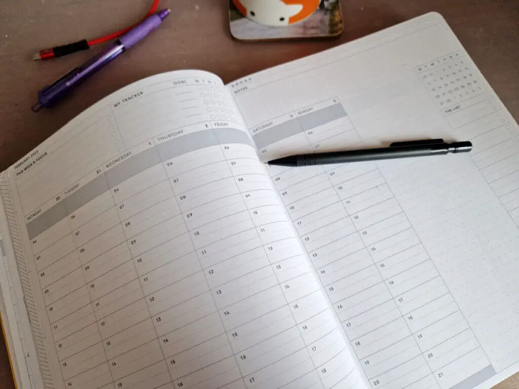 An open planner showing a blank page spread. There's a black pencil lying across the pages