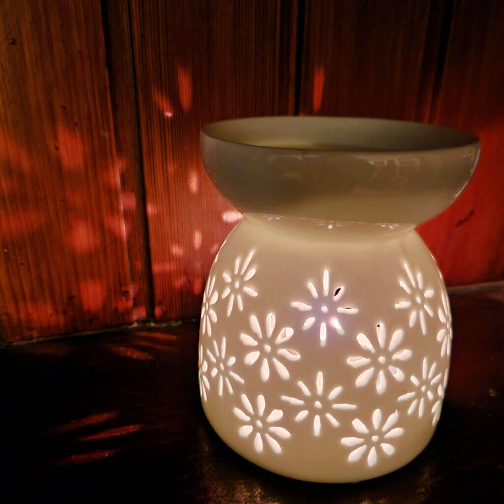 A tea light holder with flower-shaped cutouts, throwing shadows onto the wooden wall behind