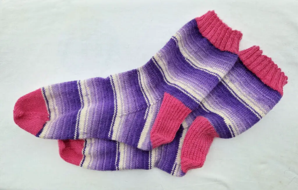 A pair of purple and white socks with pink cuffs, heels and toes lie on a white background