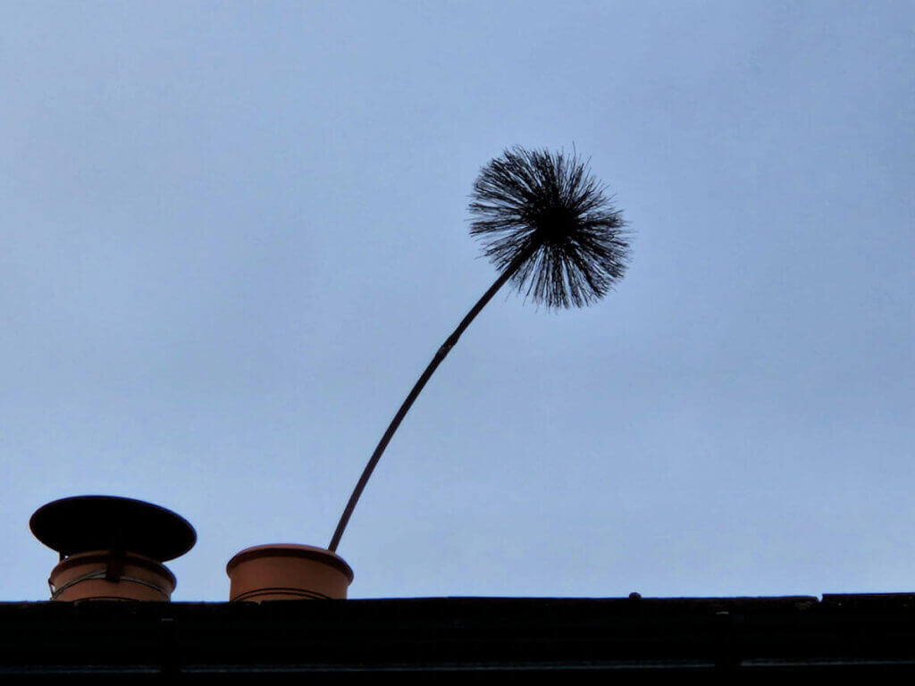 A round chimney sweep brush is poking out of the top of chimney pot. The sky behind is grey.