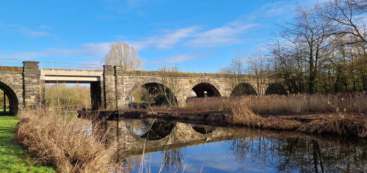 A bright blue sky reflected into a canal along with an arch railway bridge which makes circles in the reflections