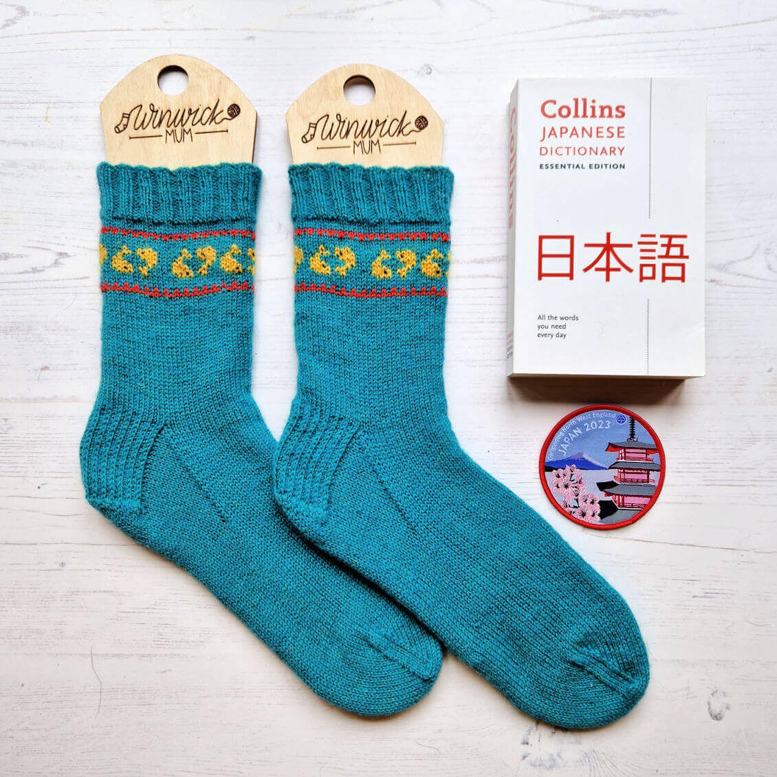 A pair of blue socks with a band of goldfish inside a red border. To the right is a Japanese dictionary and a Girl Guide camp blanket badge