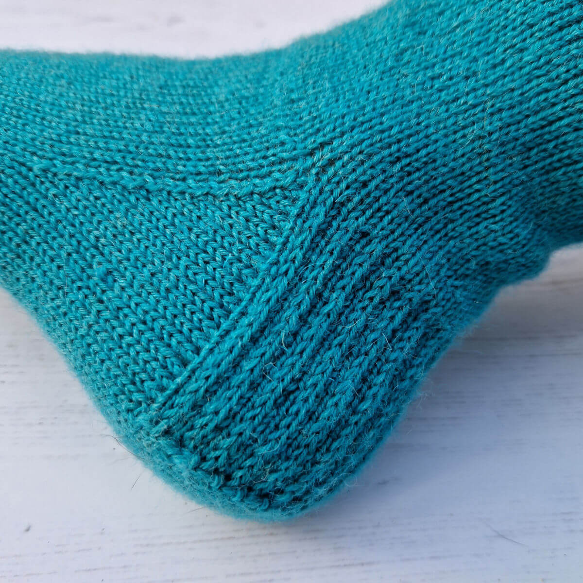 A close up of a knitted heel flap and gusset in green/blue yarn